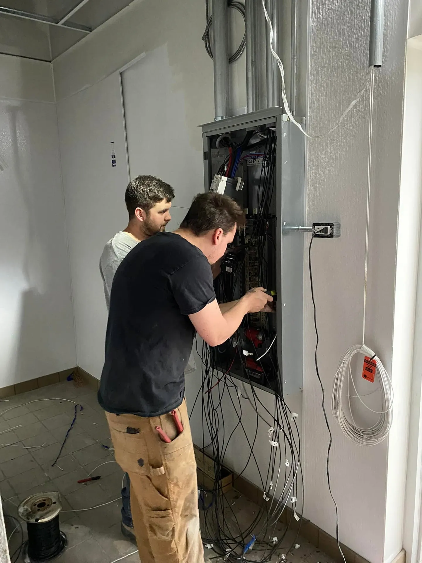 Two electricians wiring a commercial electrical panel during installation.