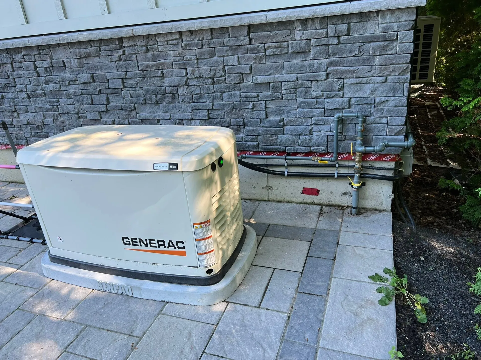 Generac standby generator installed beside a stone-clad home.