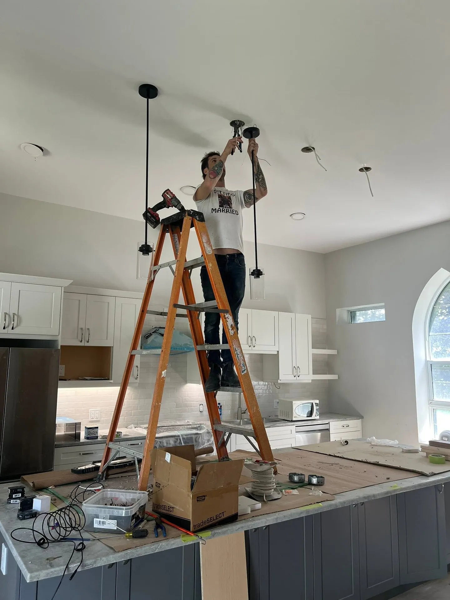 Electrician installing pendant lights above a kitchen island.