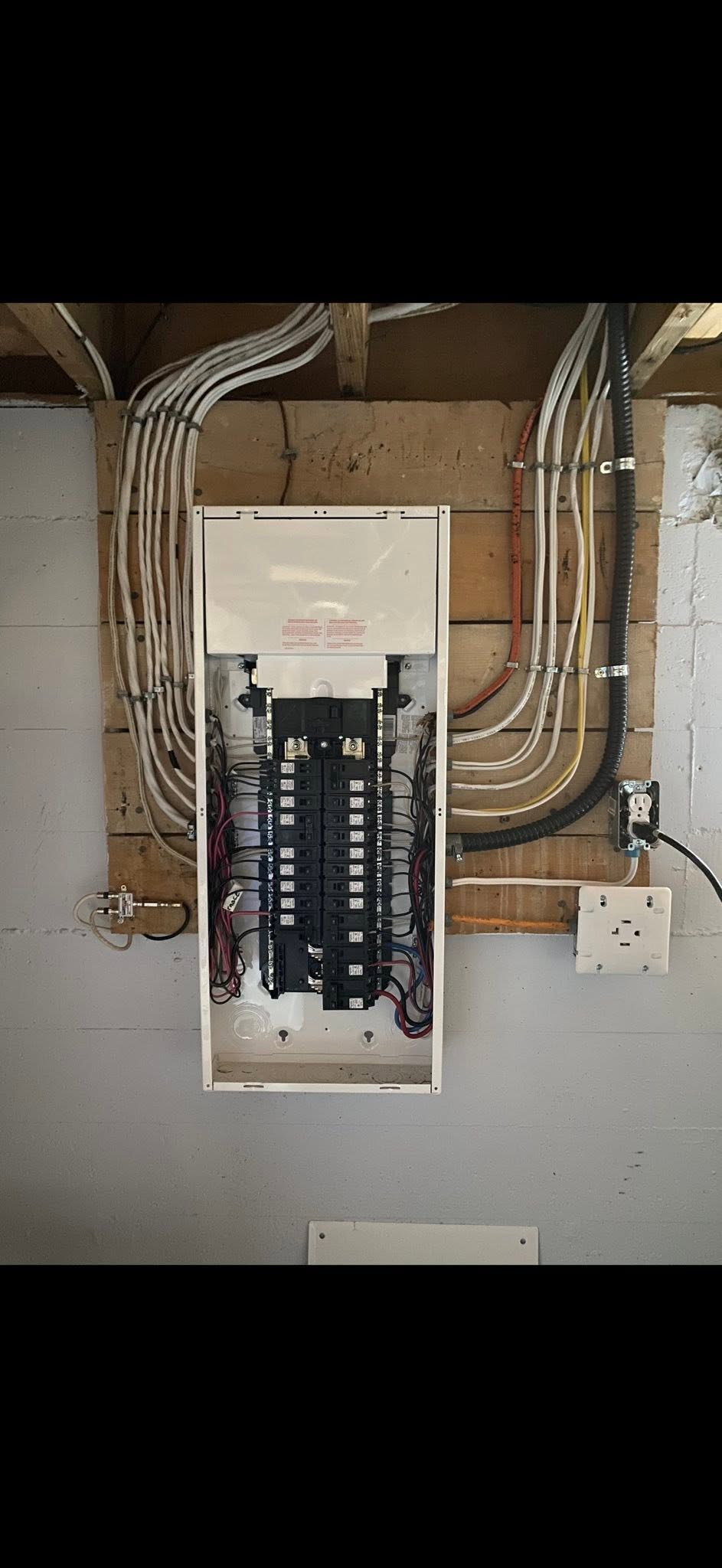 Residential breaker panel with neatly routed feeder and branch wiring on a plywood backboard.