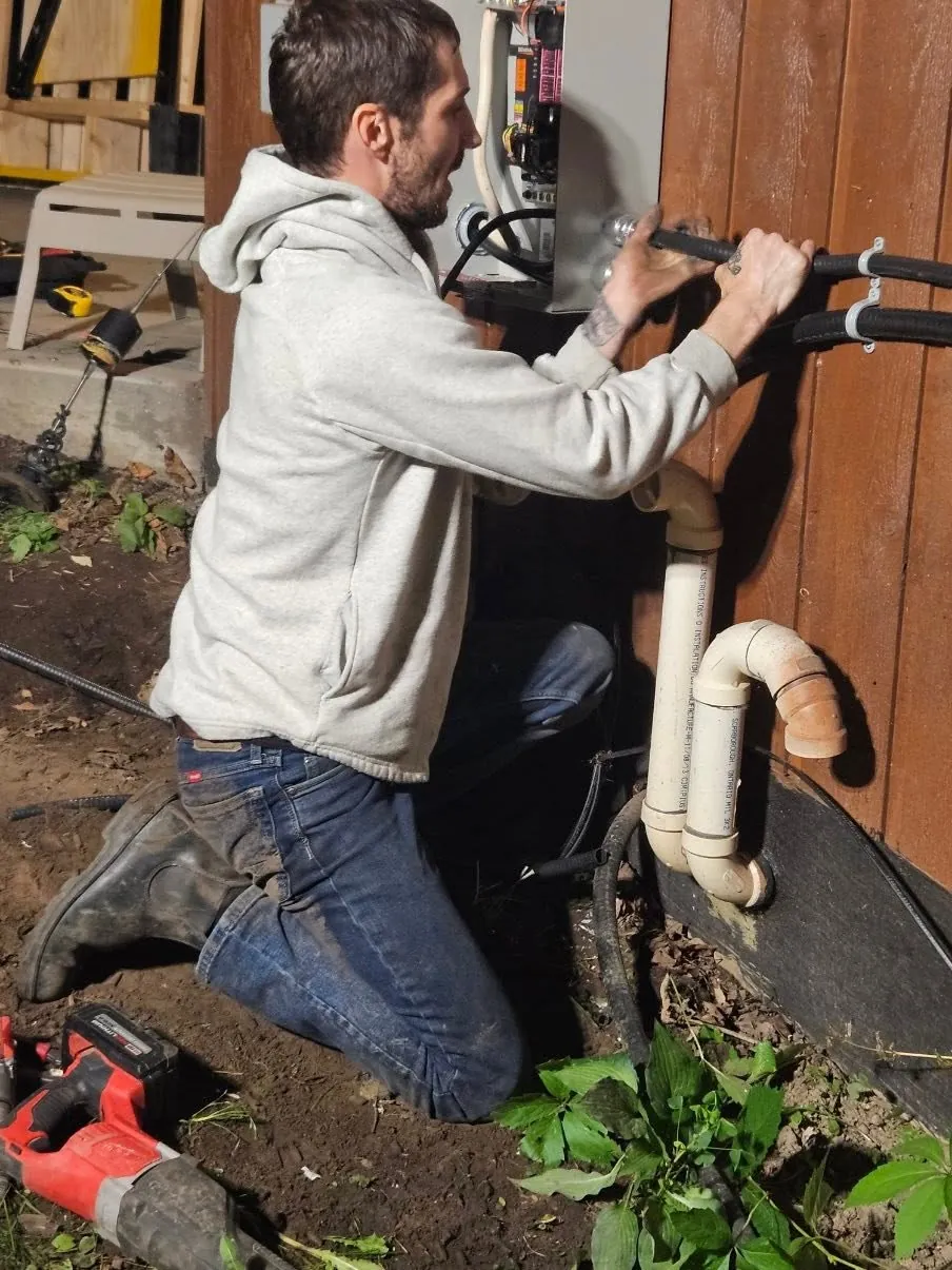 Electrician working on underground electrical service conduit beside a home.